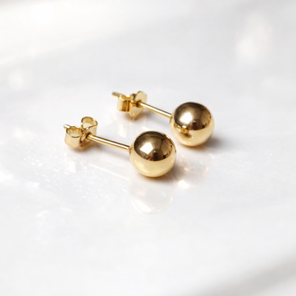 Gros plan de boucles d’oreilles boule en or massif 18 carats 750, finition polie miroir, or jaune.