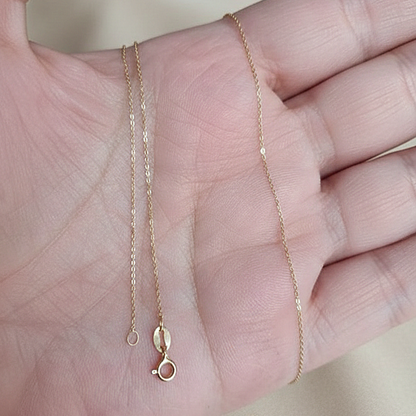 Chaîne fine maille forçat en or massif 18 carats 750 tenue en main, montrant la finesse et la souplesse.