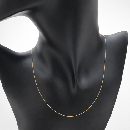 Chaîne fine maille forçat en or massif 18 carats 750 portée sur buste noir, mettant en valeur l’or jaune poli.