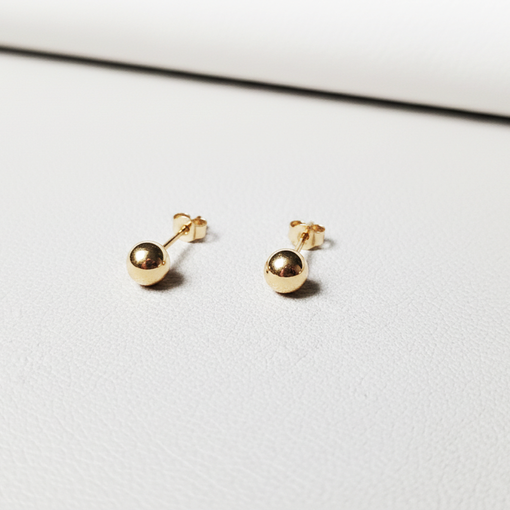 Petites puces d’oreilles boule en or massif 18 carats 750 en or jaune poli, présentées sur support métal.