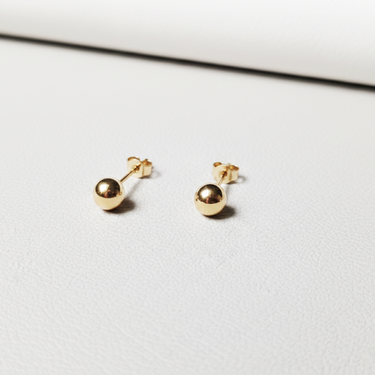 Petites puces d’oreilles boule en or massif 18 carats 750 en or jaune poli, présentées sur support métal.