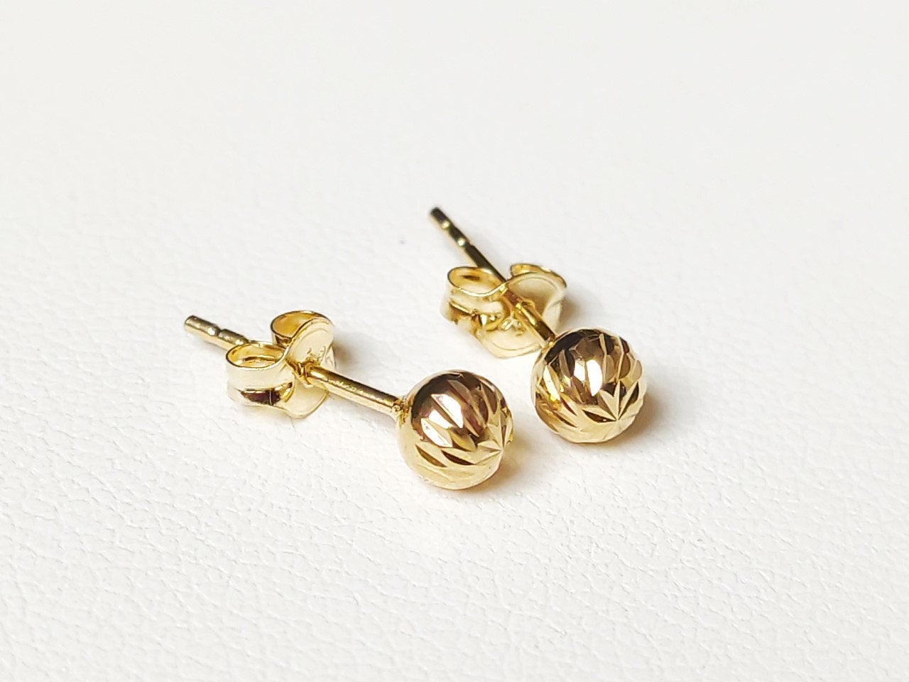 Détail de boucles d’oreilles boules ciselées en or massif 18 carats 750, finition or jaune poli.