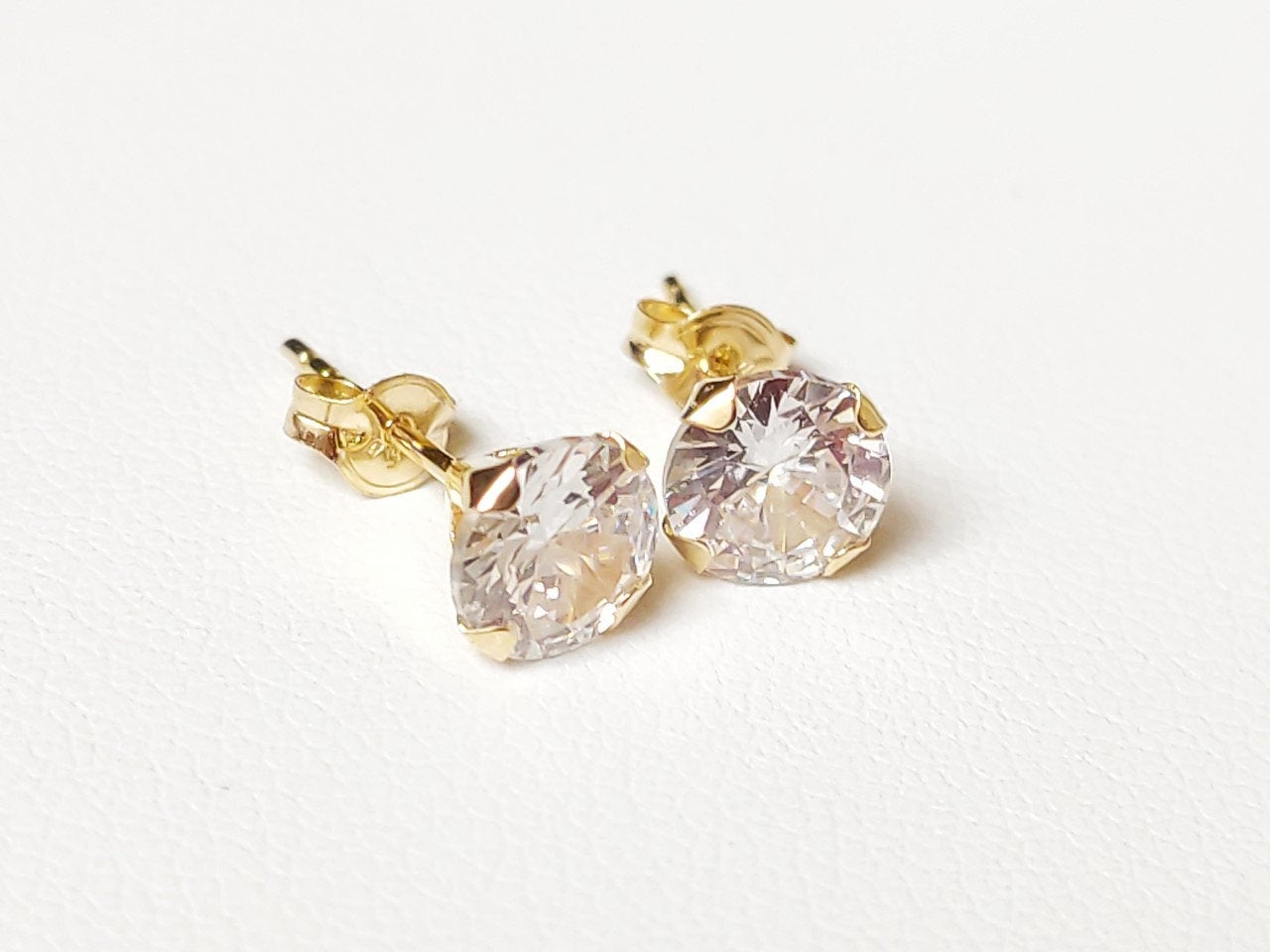 Détail de boucles d’oreilles puces en or massif 18 carats 750 avec pierre ronde transparente.